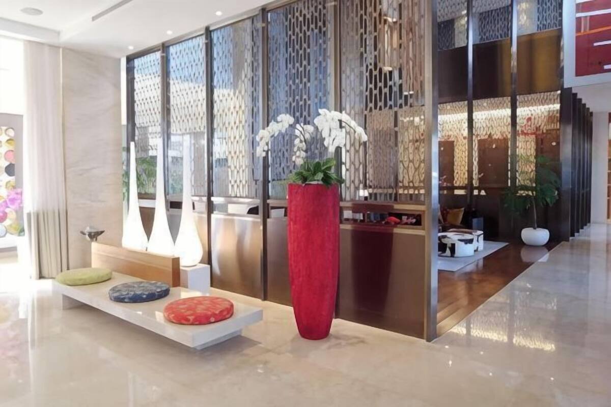 Un área de recepción con un mostrador, un jarrón rojo grande con flores blancas y una zona de estar con cojines.