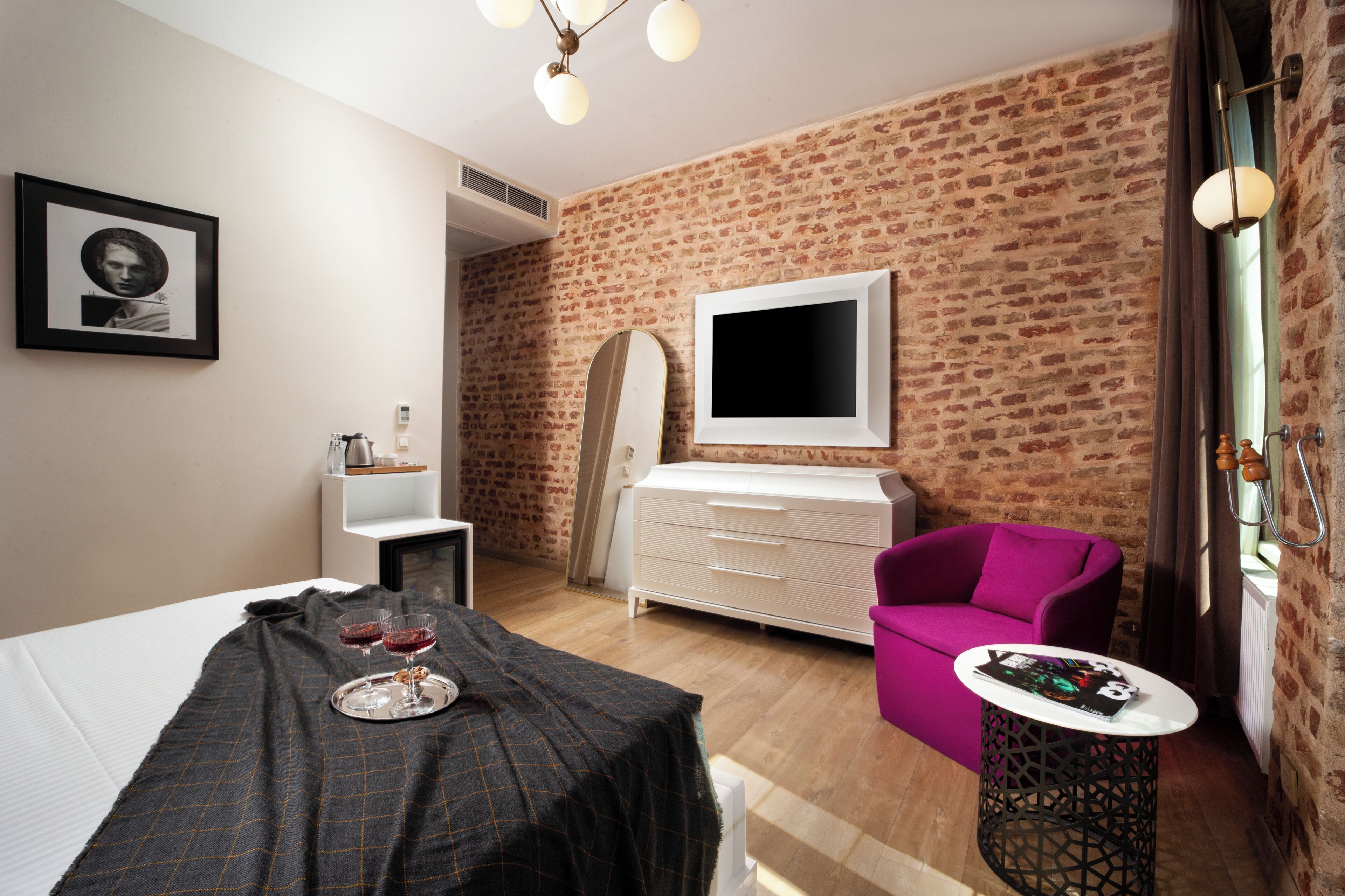 Une chambre d’hôtel avec un lit, une petite table avec des verres, une chaise, une commode et un mur en briques.