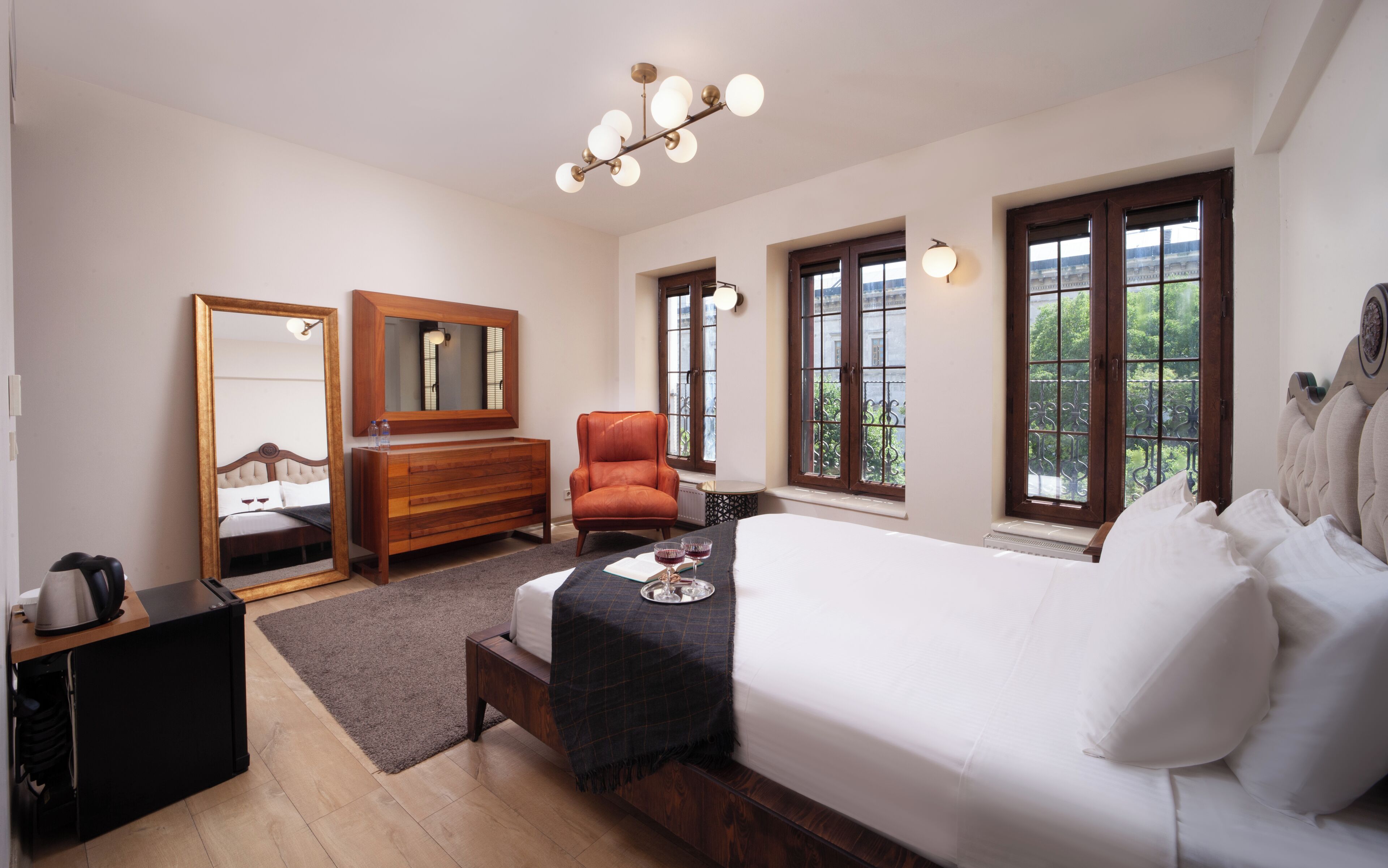 A hotel room with a bed, a dresser, a chair, a mirror, and a window with a view.
