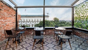 A balcony with three tables and chairs, a patterned floor, and a view of a building with a flag.