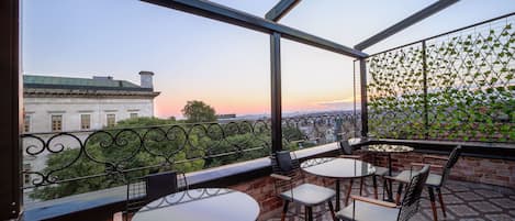 Un balcón con mesas y sillas, vista a edificios y una valla con vegetación.