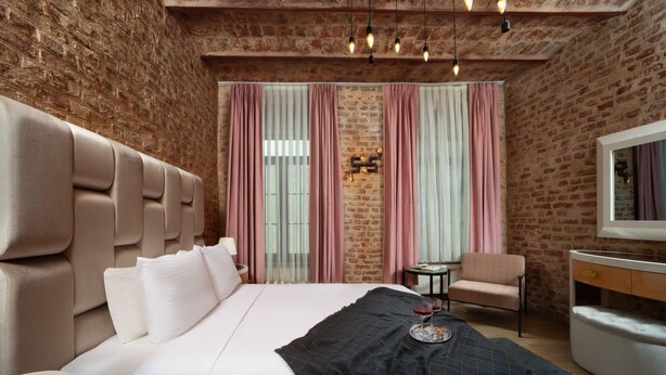 A modern hotel room with a brick wall, a large bed with a headboard, a small table, a chair, and a vanity with a mirror. - Nine Istanbul Hotel (Istanbul)
