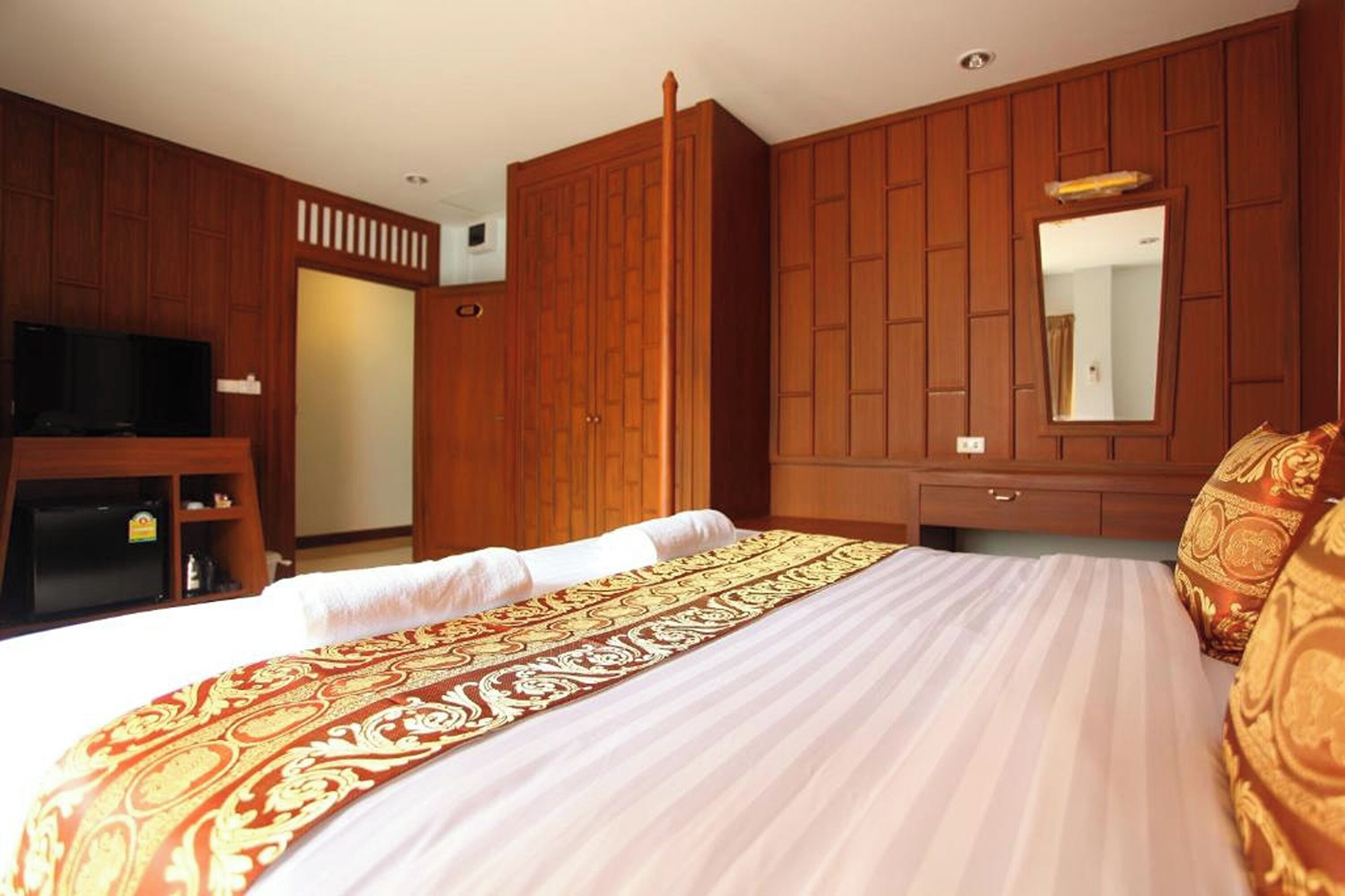Quarto de hotel com uma cama grande, painéis de madeira, uma televisão e um espelho.