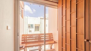 A room with a sliding glass door leading to an outdoor area with a wooden bench and a view of buildings. - Lotus Hotel Patong (Patong)