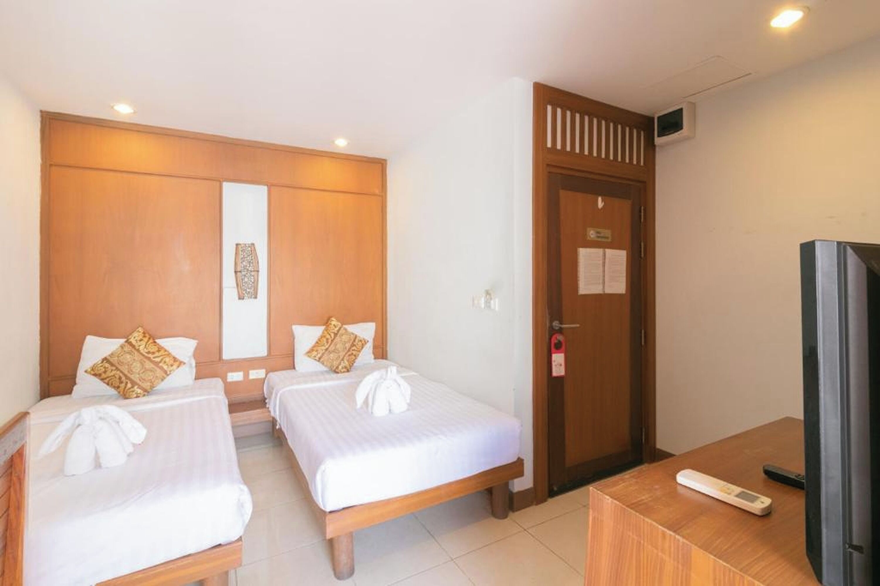 A hotel room with two single beds, a wooden wardrobe, a television, and a small table.