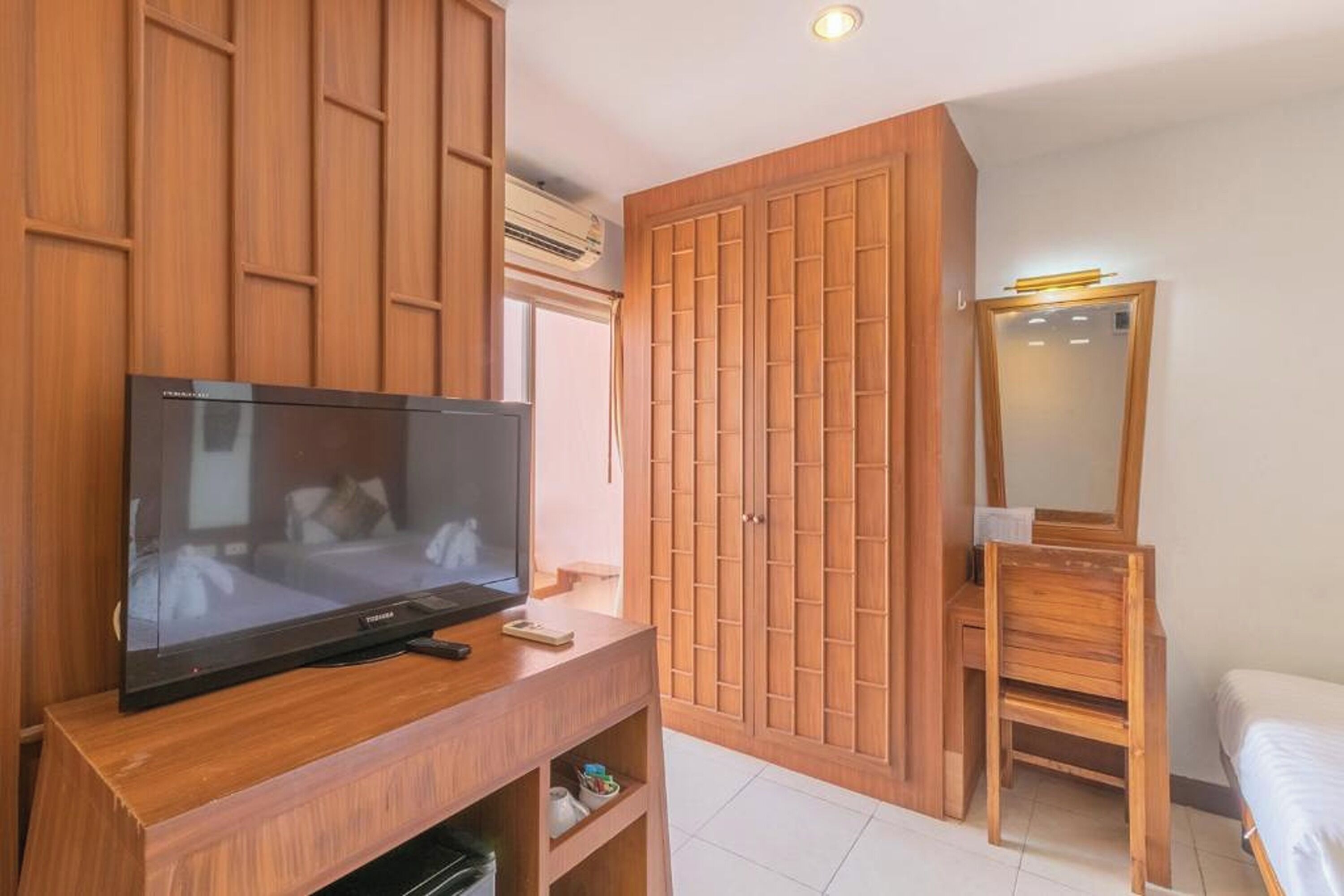 Una habitación con televisor sobre un soporte de madera, un armario, un espejo y una cama.