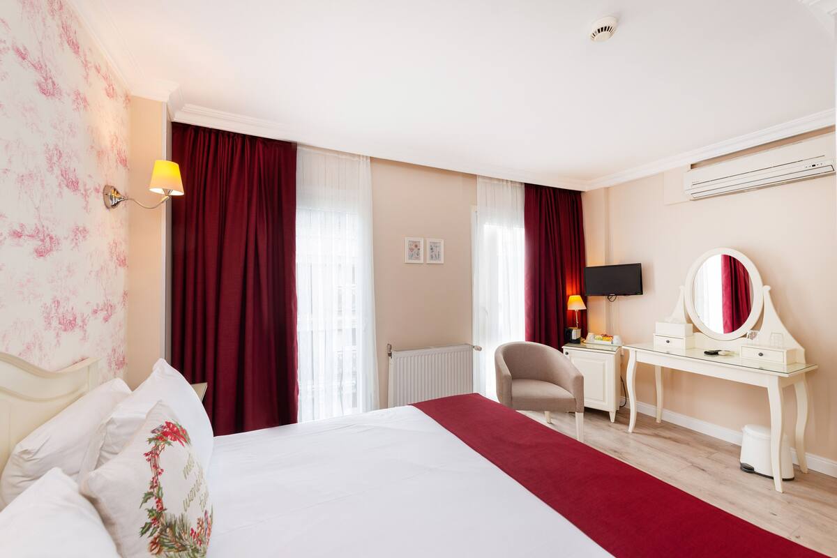 Una habitación de hotel con cama, escritorio, silla, televisión y radiador.