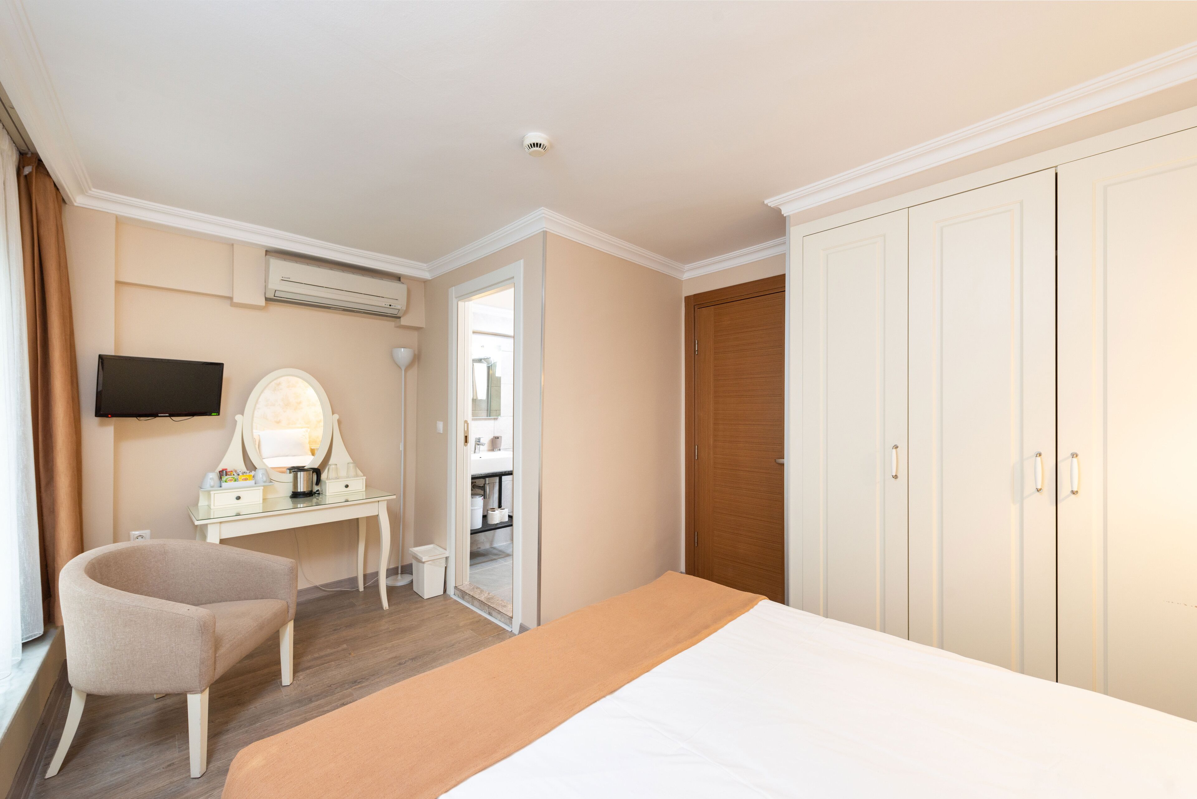 A hotel room with a bed, a desk with a mirror, a television, and a wardrobe.