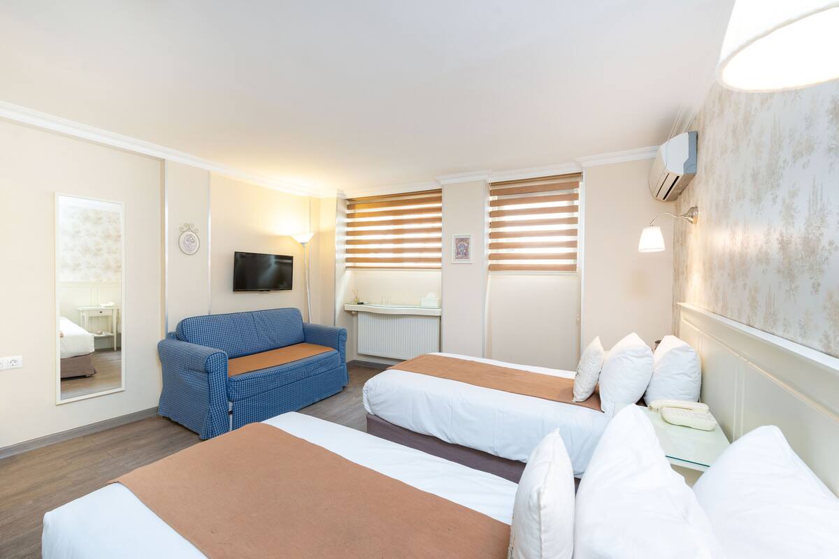 Habitación de hotel con dos camas, un sofá, un televisor y un espejo.