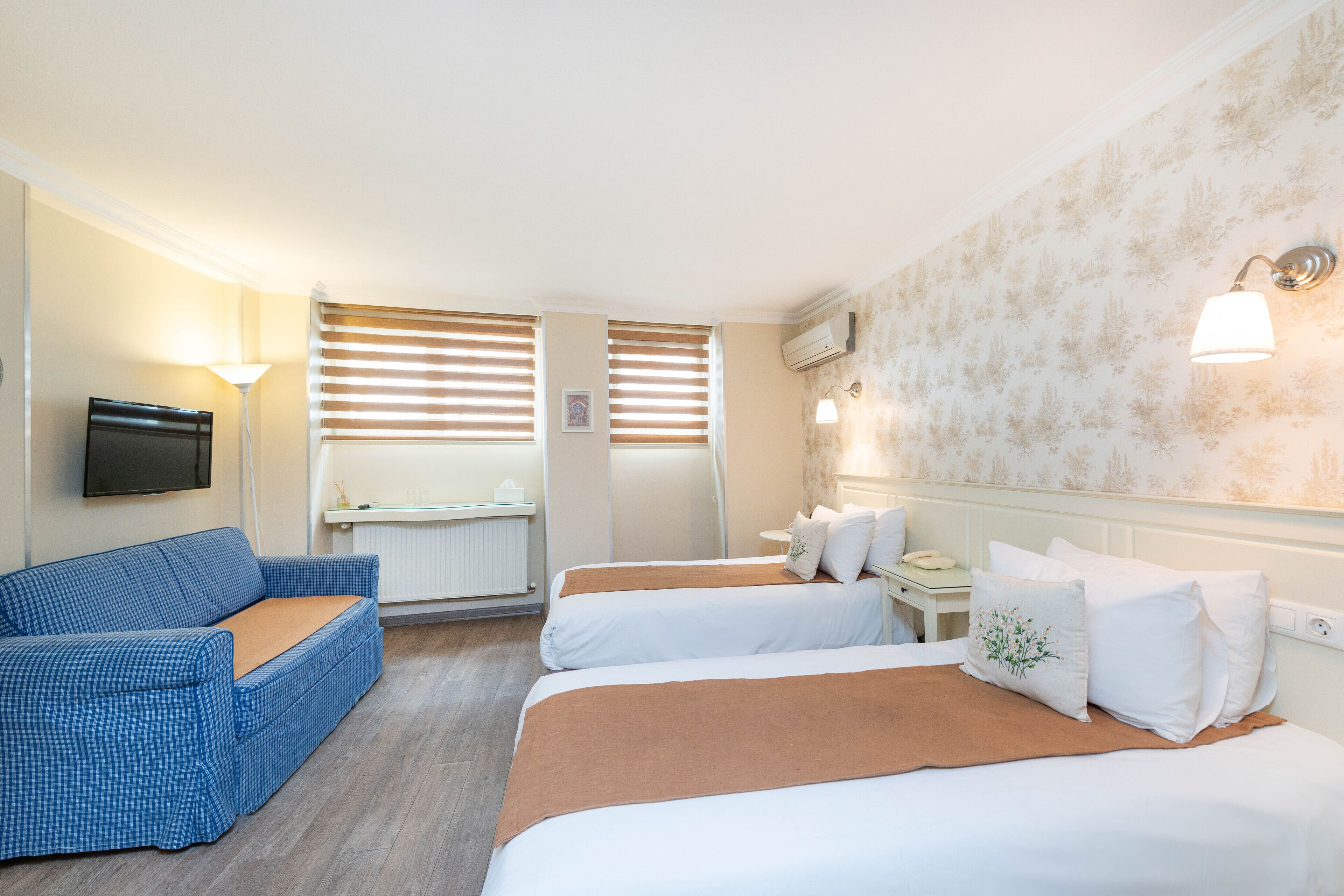 Habitación de hotel con dos camas, un sofá, un televisor y una ventana con persianas.