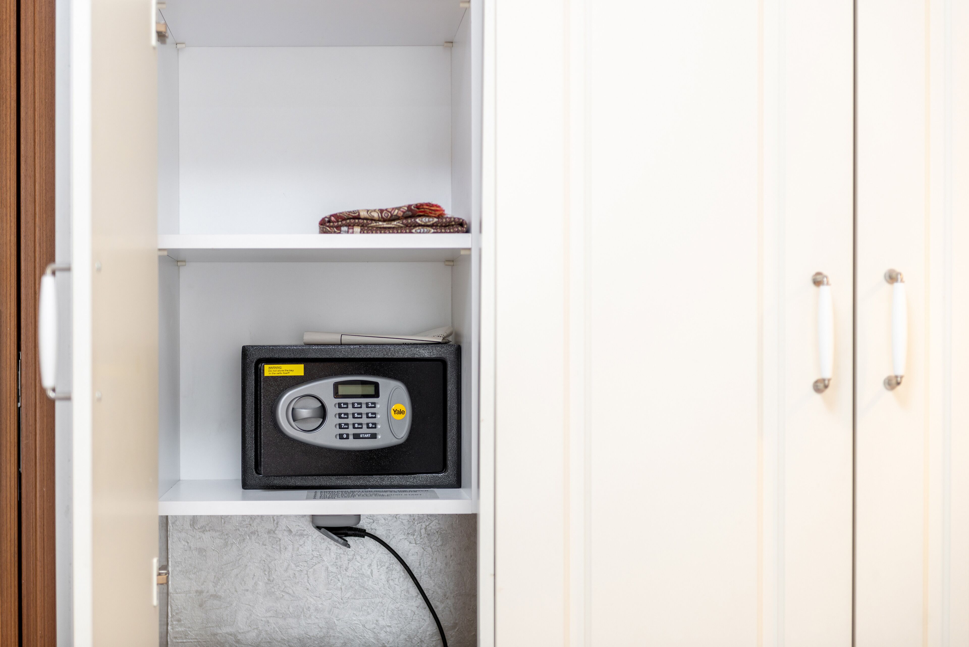 A white cabinet with a safe on the middle shelf and a patterned item on the top shelf.