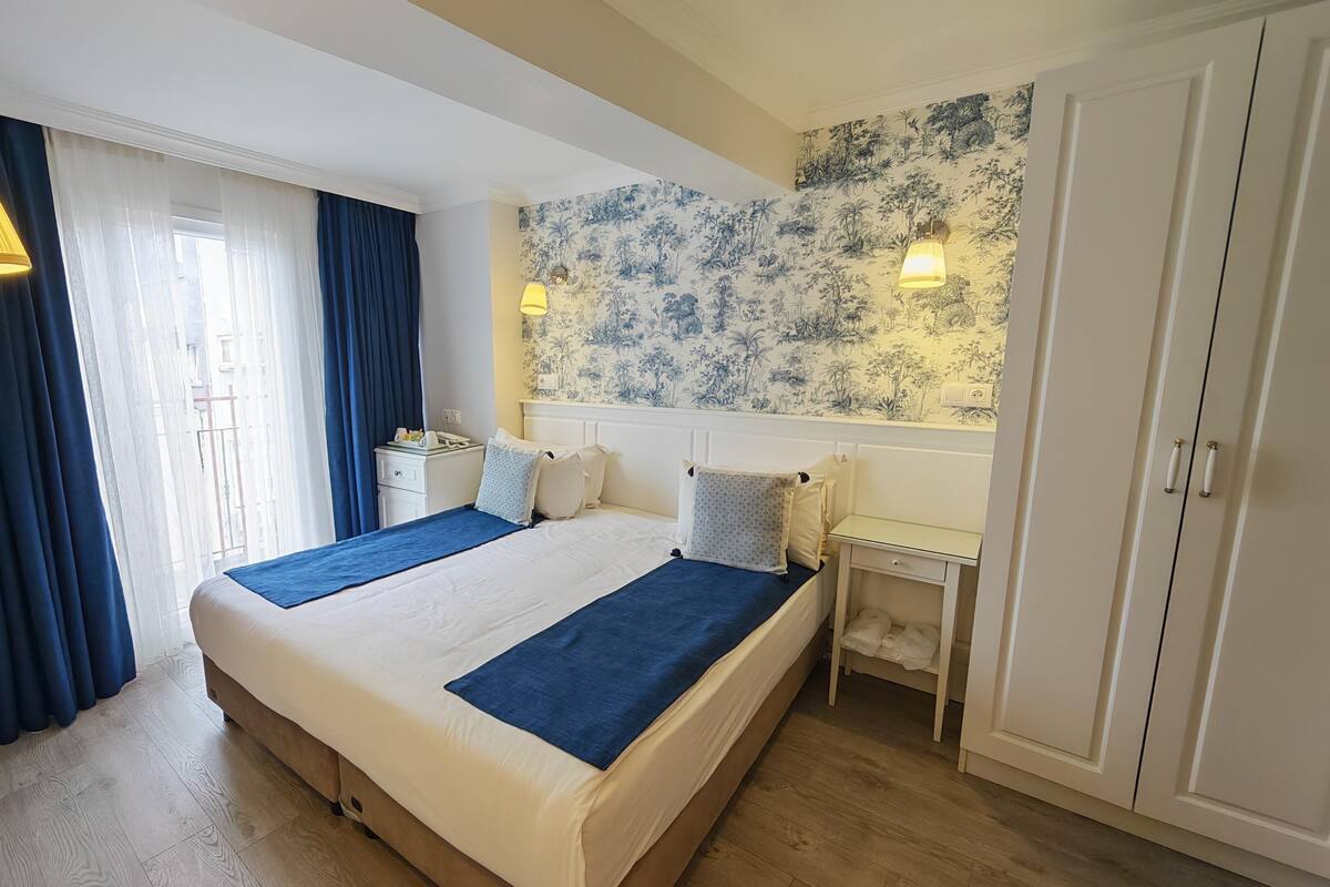 Habitación de hotel con una cama grande, una mesita de noche, un armario y una ventana con cortinas.