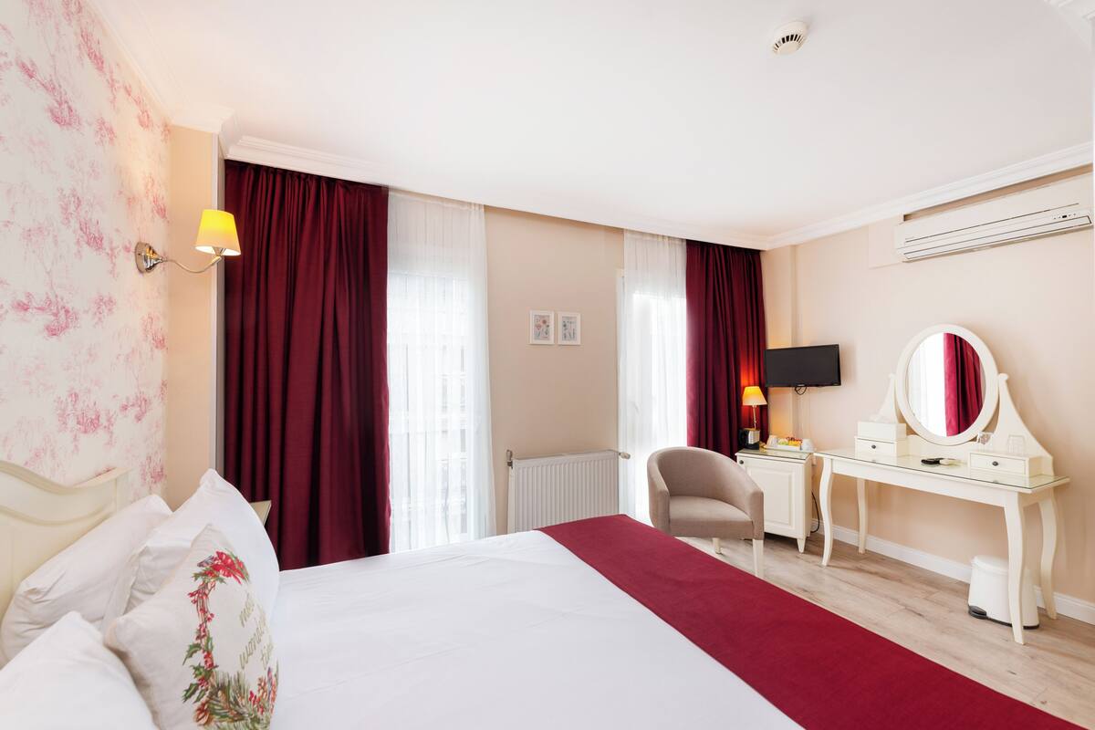 Una habitación de hotel con cama, escritorio, silla, televisión y radiador.