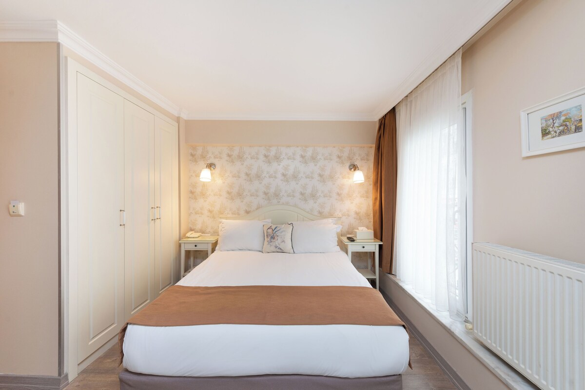 A neatly arranged hotel room with a large bed, two bedside tables, and a headboard with wall-mounted lights.