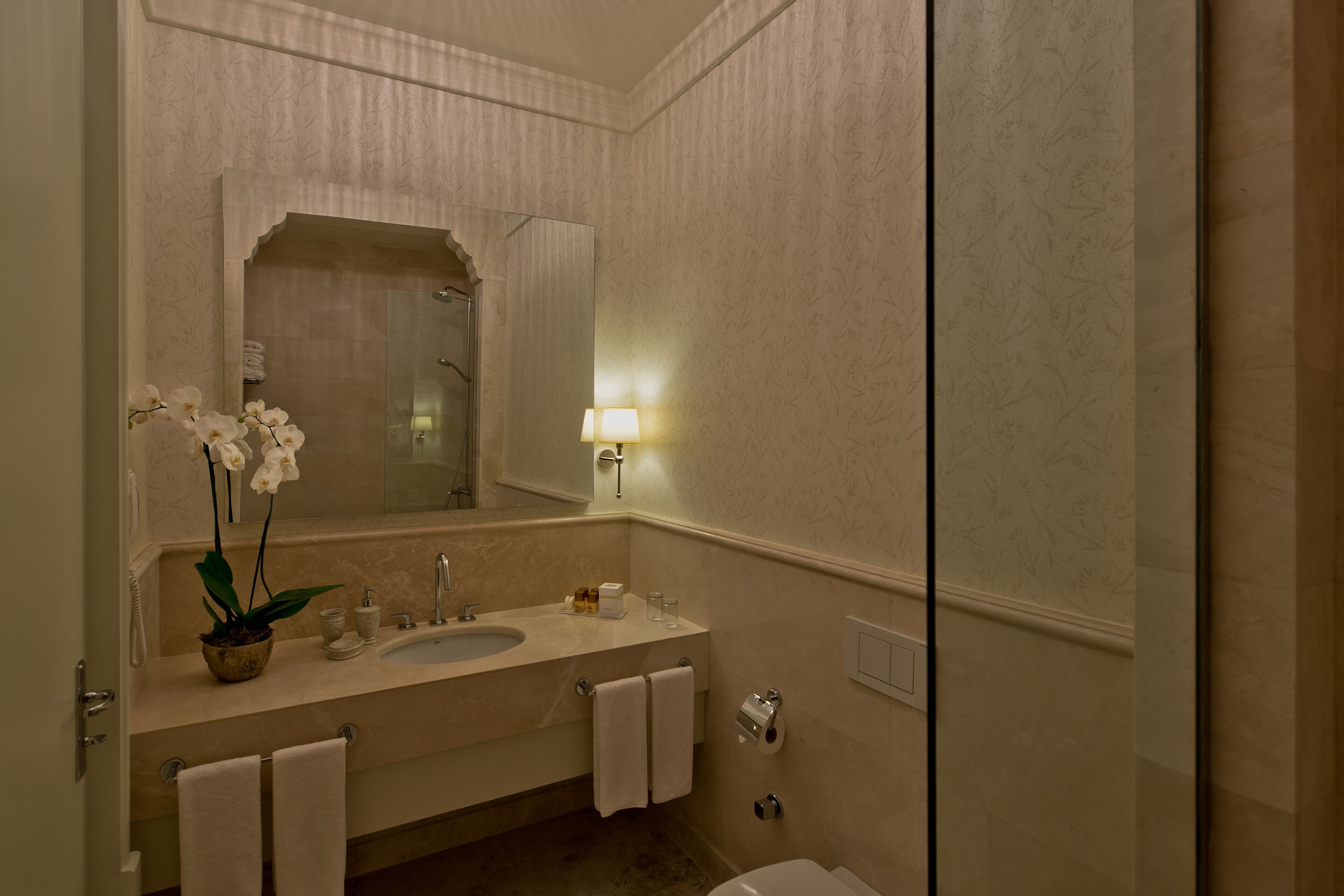 A bathroom with a sink, mirror, and a potted orchid.