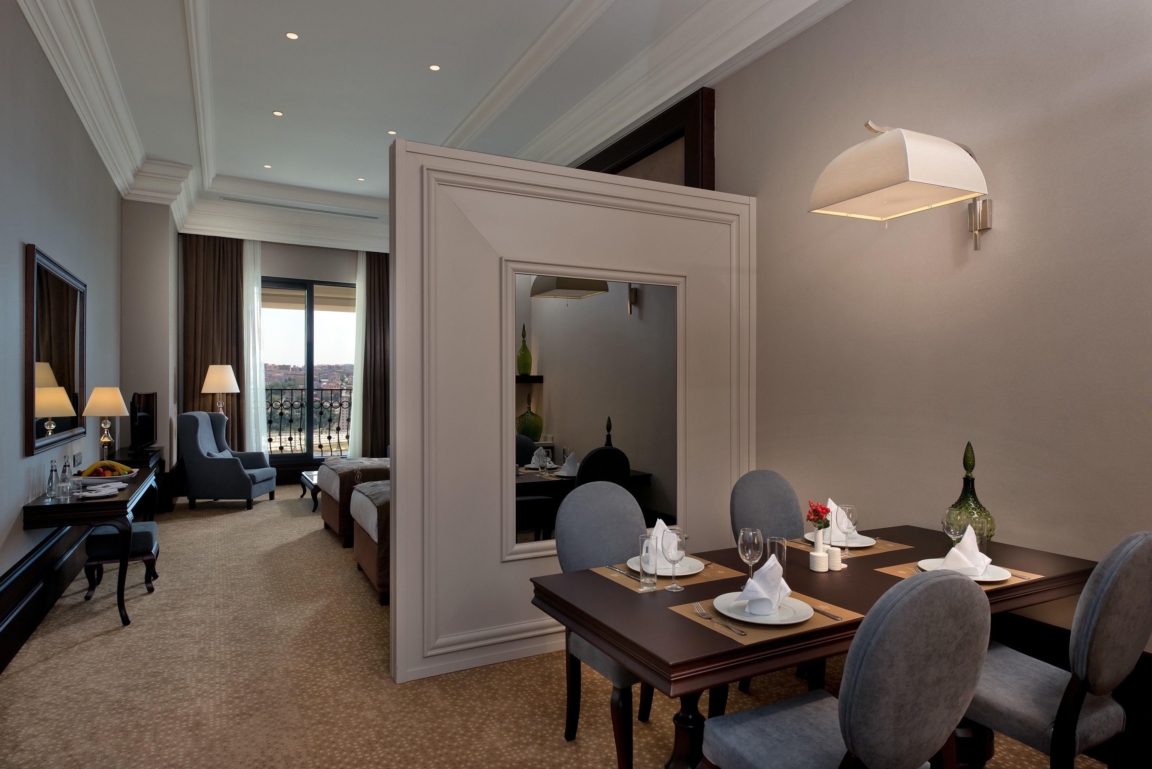 A hotel dining room with a large mirror, a dining table set for four, and a view of the city through the window.