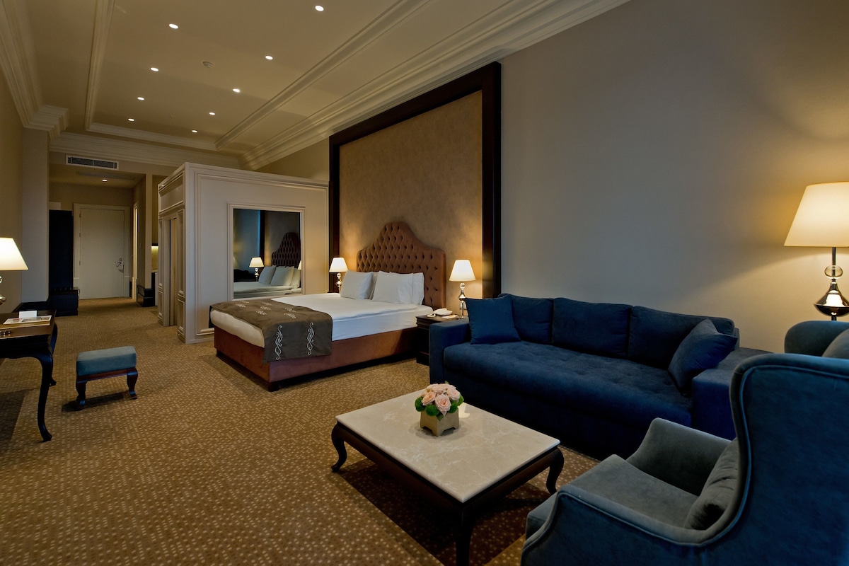 A hotel room with a large bed, a blue sofa, a small table with a vase of flowers, and two bedside lamps.