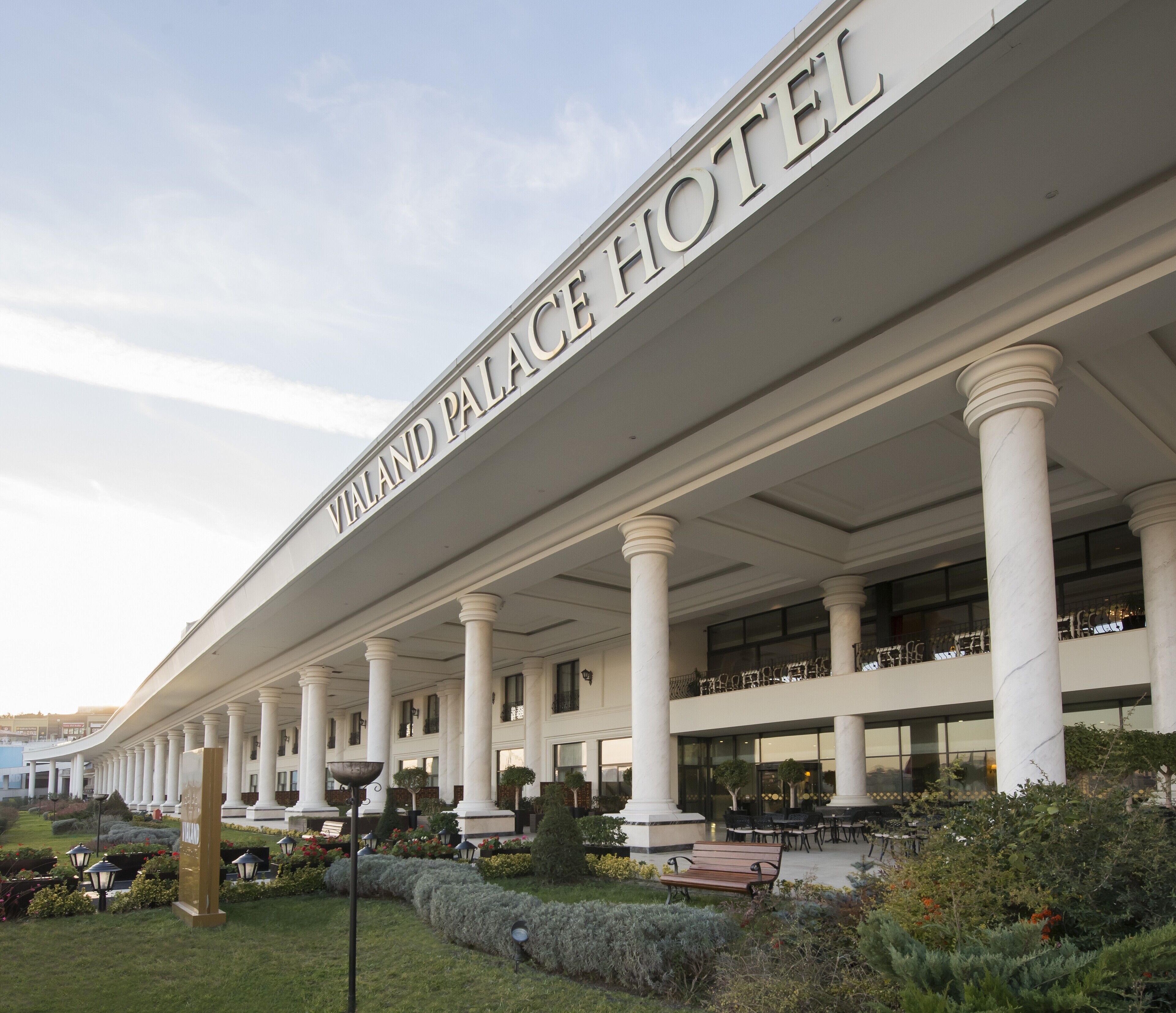 The exterior of the Vialand Palace Hotel with a series of columns, outdoor seating, and a well-maintained garden.
