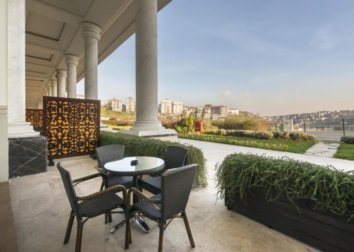 Un espacio exterior con mesas y sillas, un panel decorativo y vistas a un paisaje urbano.