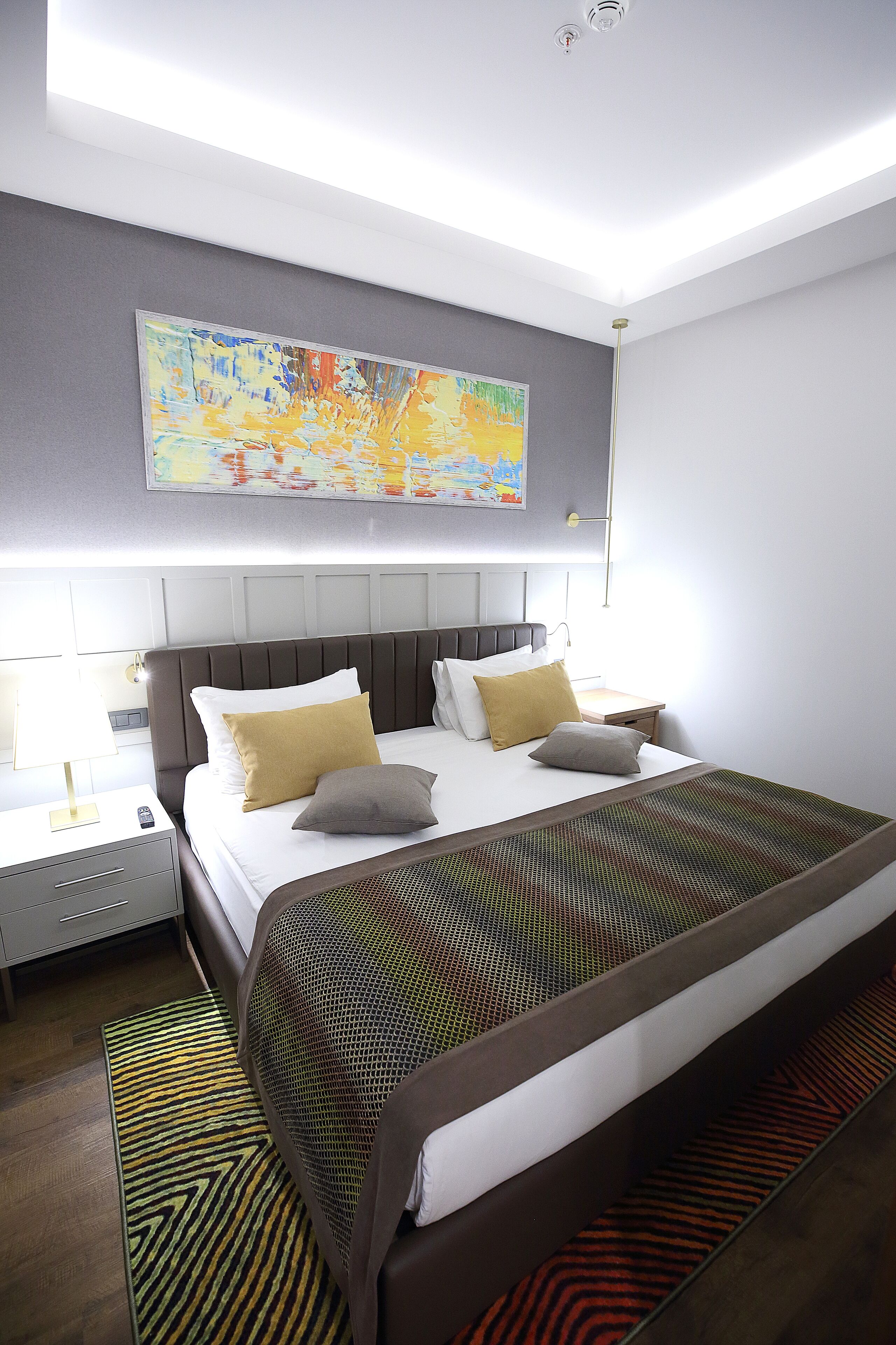 Una habitación de hotel moderna con una cama grande, una mesita de noche y un cuadro en la pared.