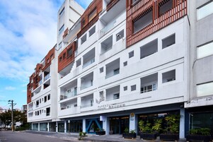 Un hotel de varios pisos con una fachada moderna, con balcones de barandillas de madera y un cartel que indica que es un hotel.