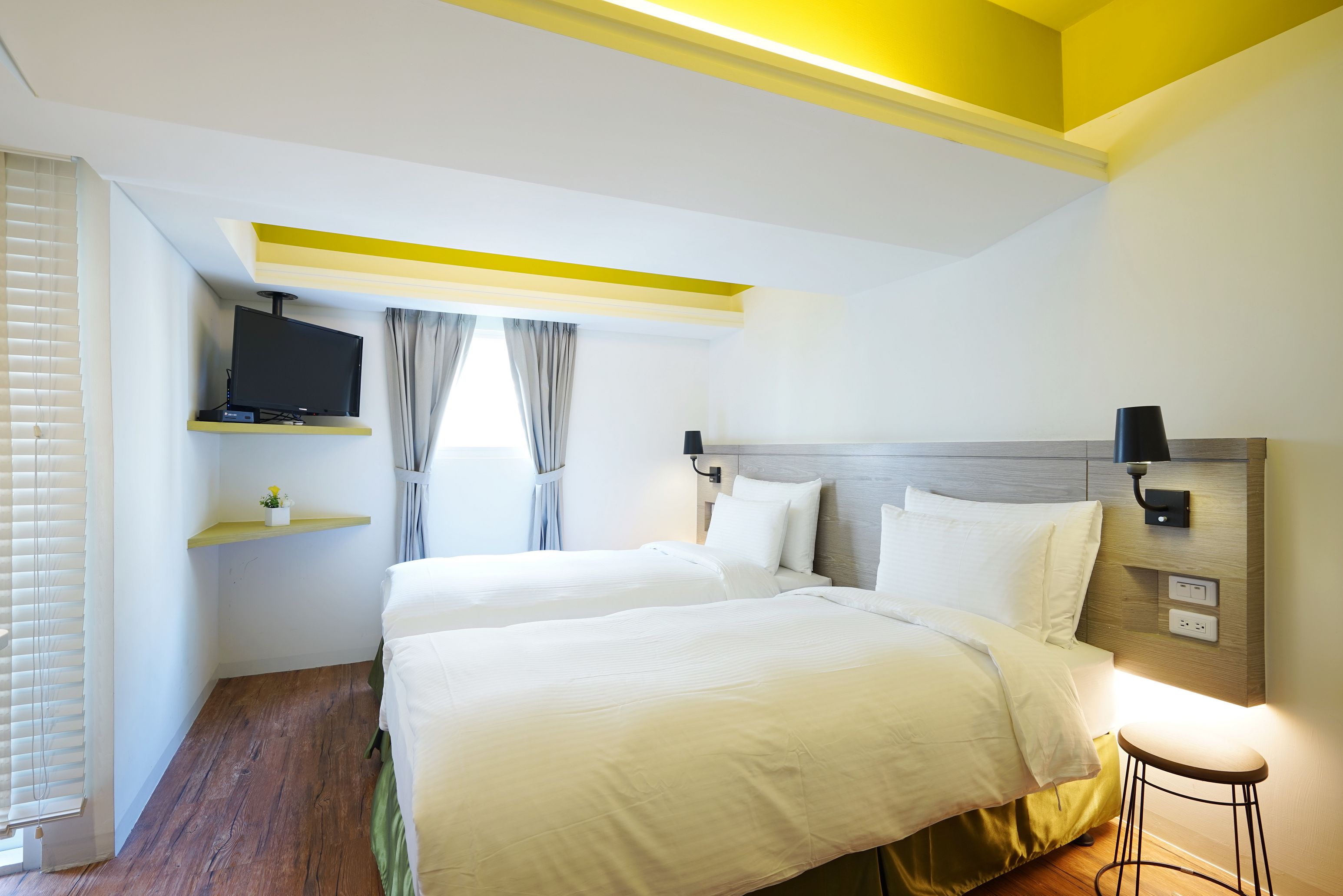 A hotel room with a large bed, a TV mounted on the wall, a small table, and a window with curtains.