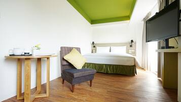 A hotel room with a bed, a television, a small table with a kettle, and a chair.