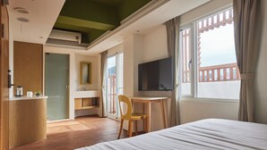 Ett hotellrum med en säng, ett skrivbord, en stol, en tv och en balkong med utsikt.