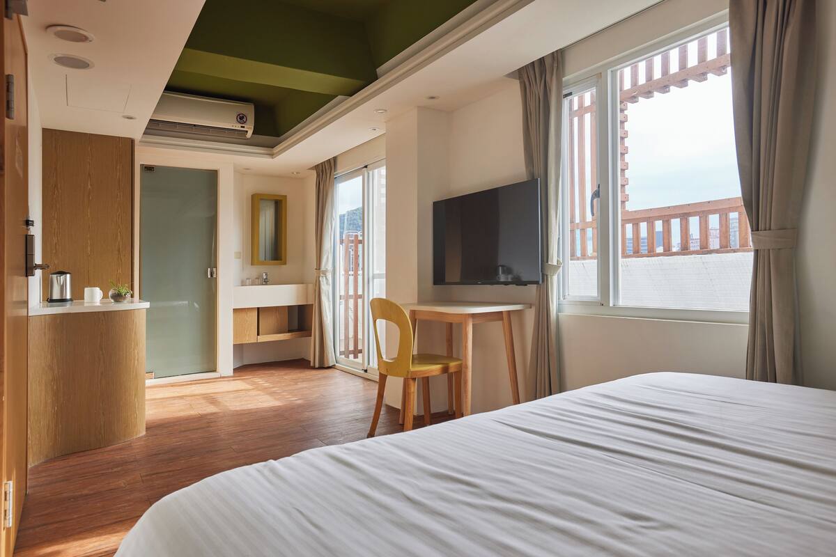 Quarto de hotel com cama, escrivaninha, cadeira, televisão e varanda com vista.