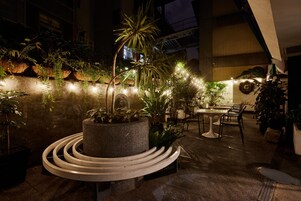 Un patio al aire libre con plantas en macetas, un espacio de estar circular y una mesa de comedor con sillas.