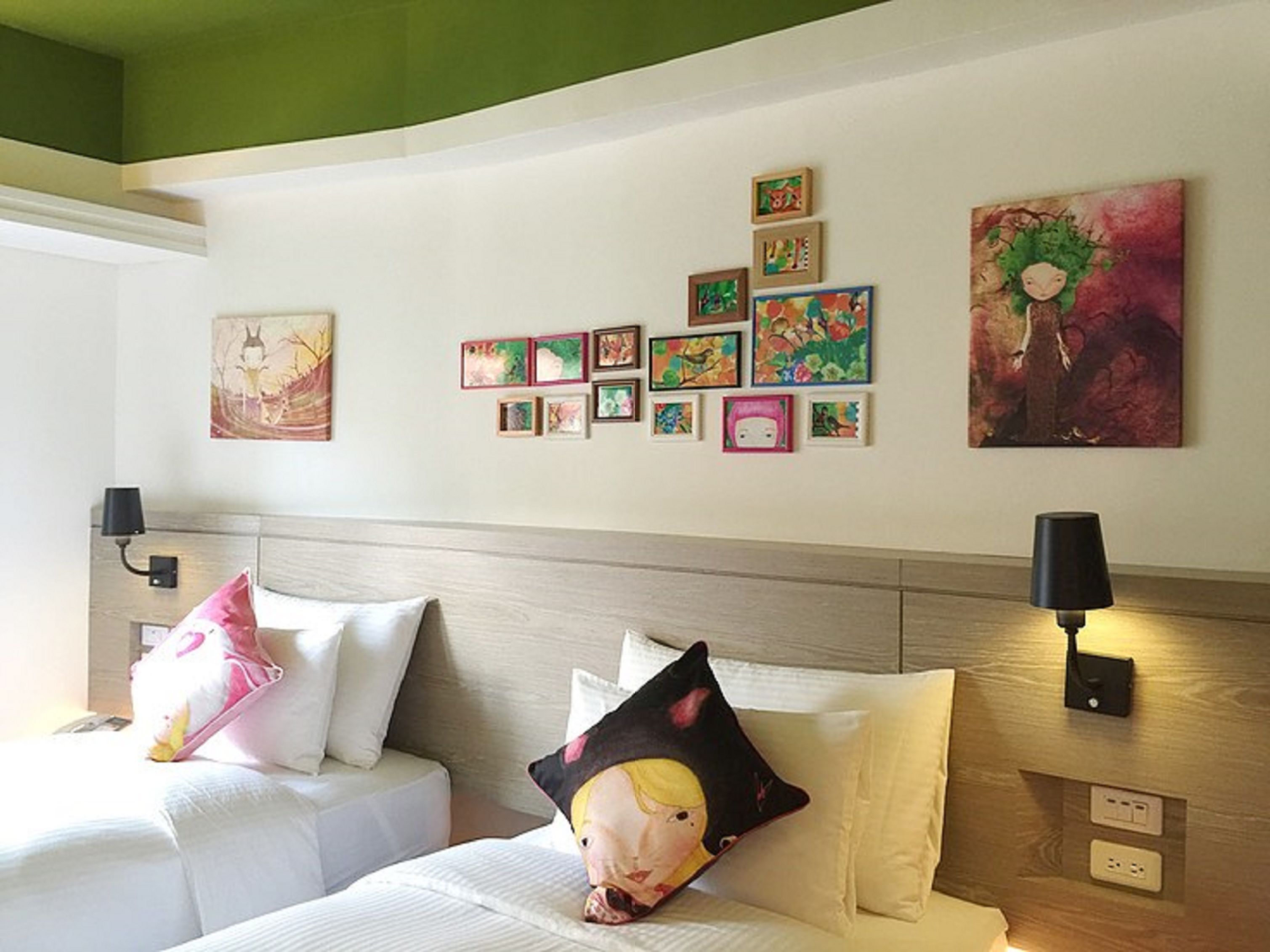 Habitación de hotel con dos camas, techo verde y una pared decorada con diversas obras de arte enmarcadas.