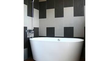 A modern bathroom with a freestanding bathtub, a showerhead, and a tiled wall with a checkered pattern.