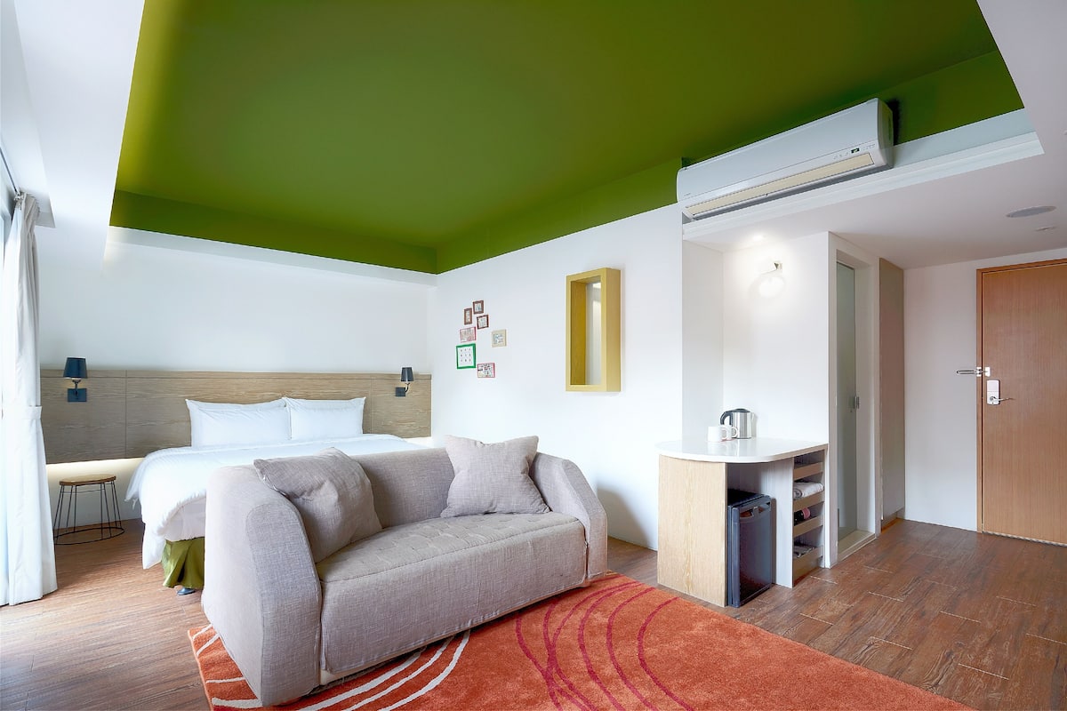 Quarto de hotel moderno com cama, sofá e cozinha compacta.