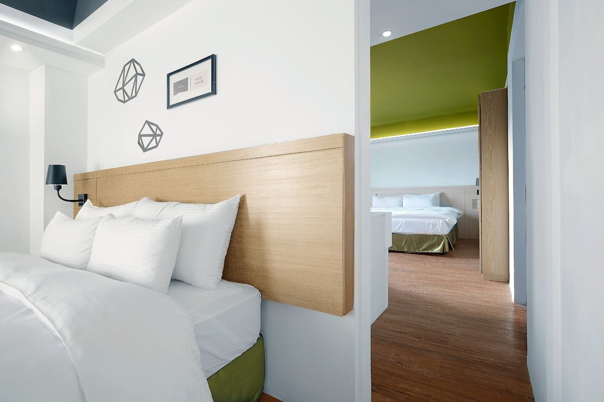 Quarto de hotel moderno com cabeceira de madeira, roupa de cama branca e arte de parede geométrica.