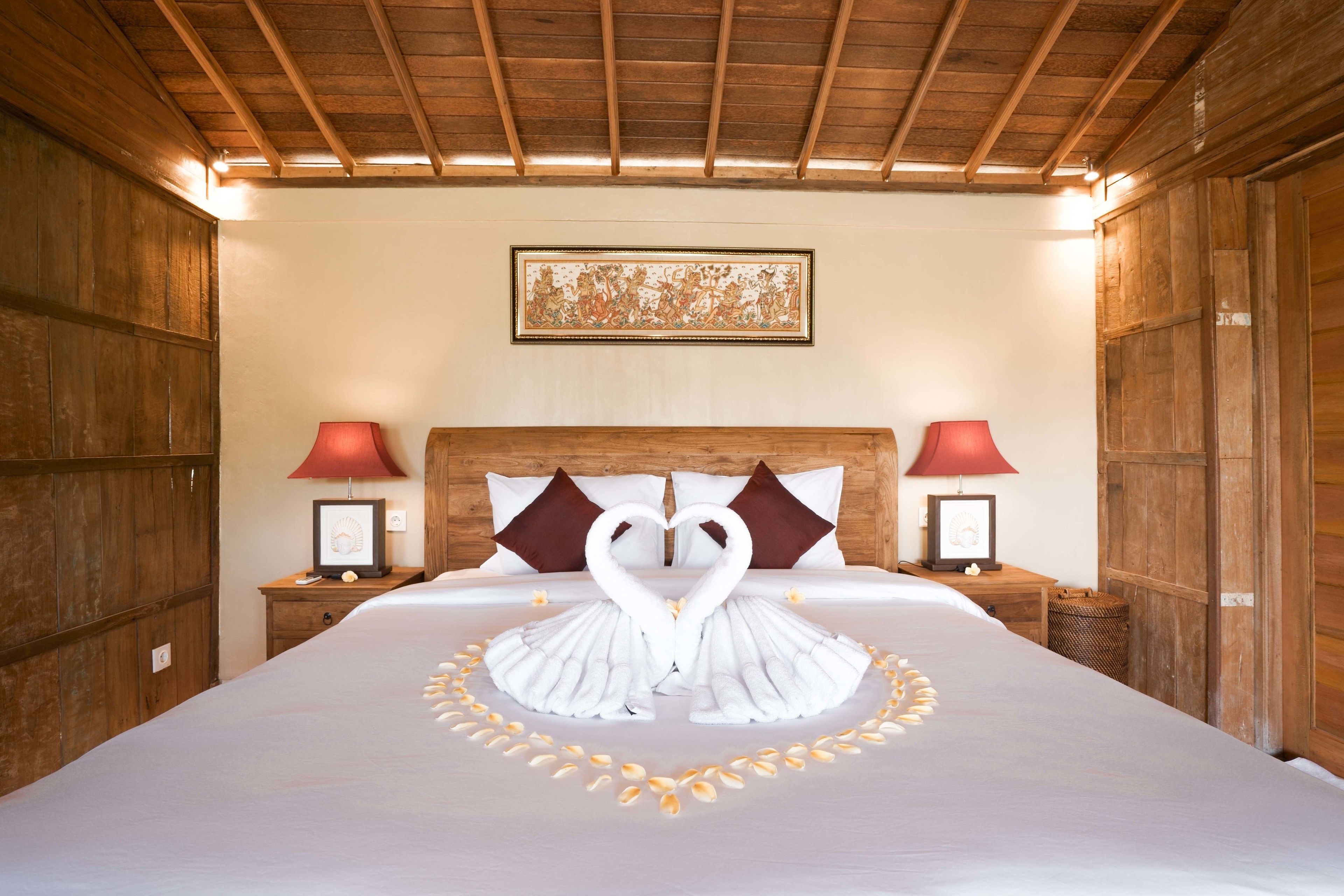A hotel room with a large bed, wooden headboard, two bedside tables with lamps, and a framed artwork on the wall.