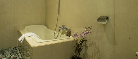 A bathroom with a bathtub, toilet, and a potted orchid.