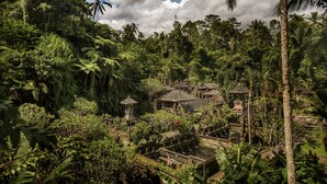 A lush, tropical garden with a variety of trees and plants, including palm trees. There are several thatched-roof structures, possibly huts or gazebos, scattered throughout the garden. - Pondok Sebatu Villa (Sebatu)
