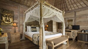 A four-poster bed with a canopy, wooden flooring, a bedside table with a lamp, a mirror, and a small table with a bench. - Pondok Sebatu Villa (Sebatu)