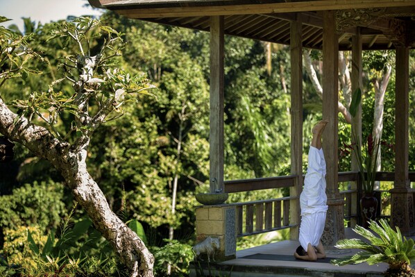 A person performing a yoga pose on a wooden platform with a lush green background. - Pondok Sebatu Villa (Sebatu)