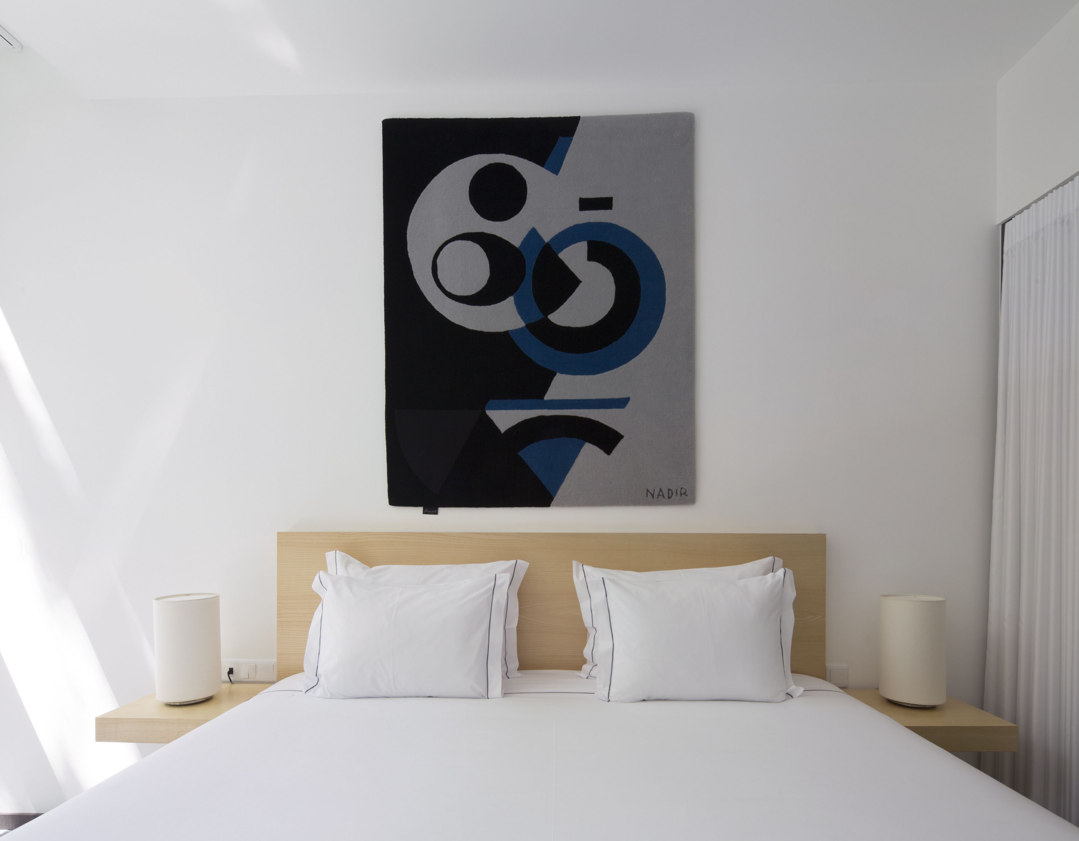 Una habitación de hotel moderna con un cuadro abstracto grande en la pared, una cama bien hecha con ropa blanca y dos lámparas de noche.