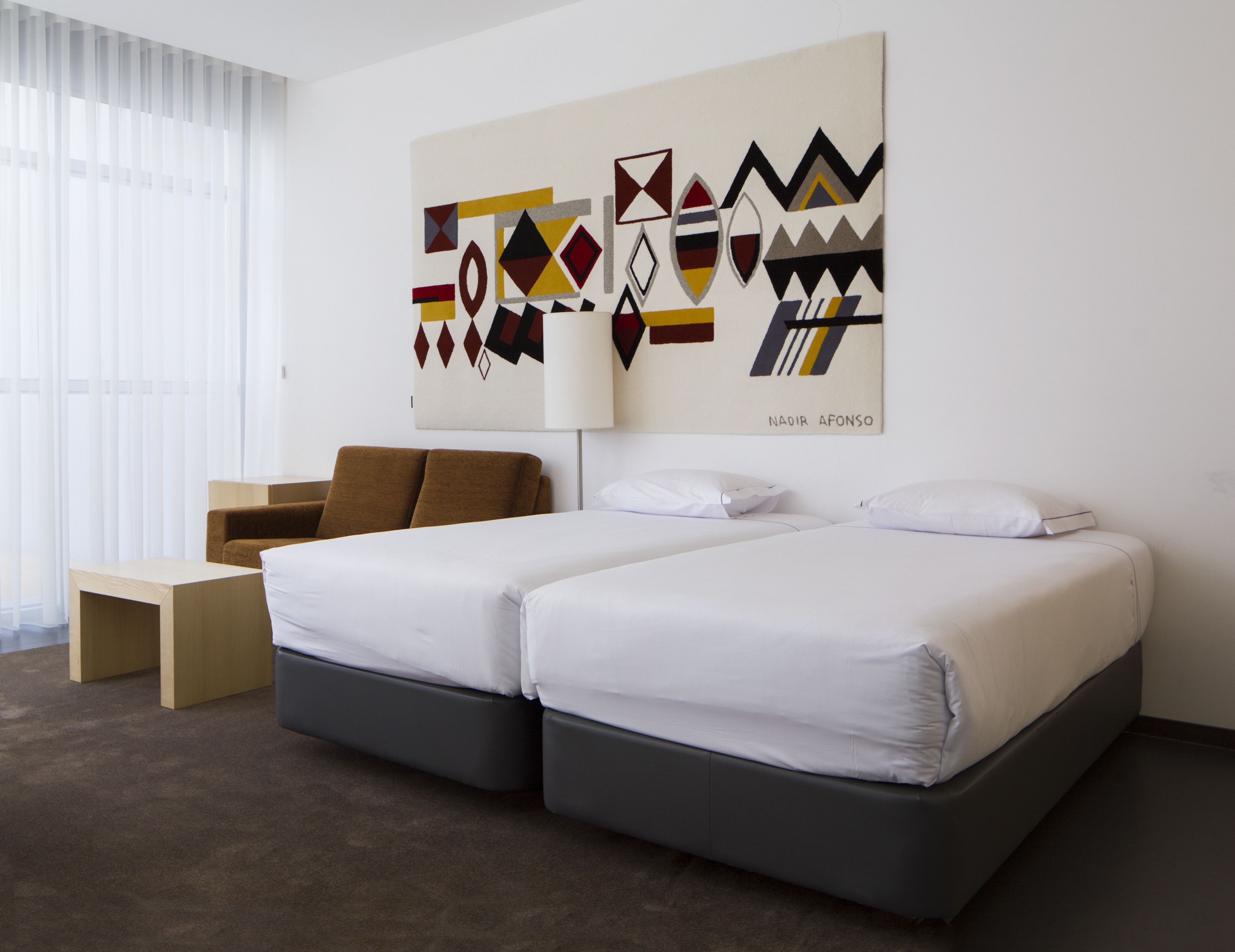 A hotel room with two beds, a desk, and a large abstract painting on the wall.