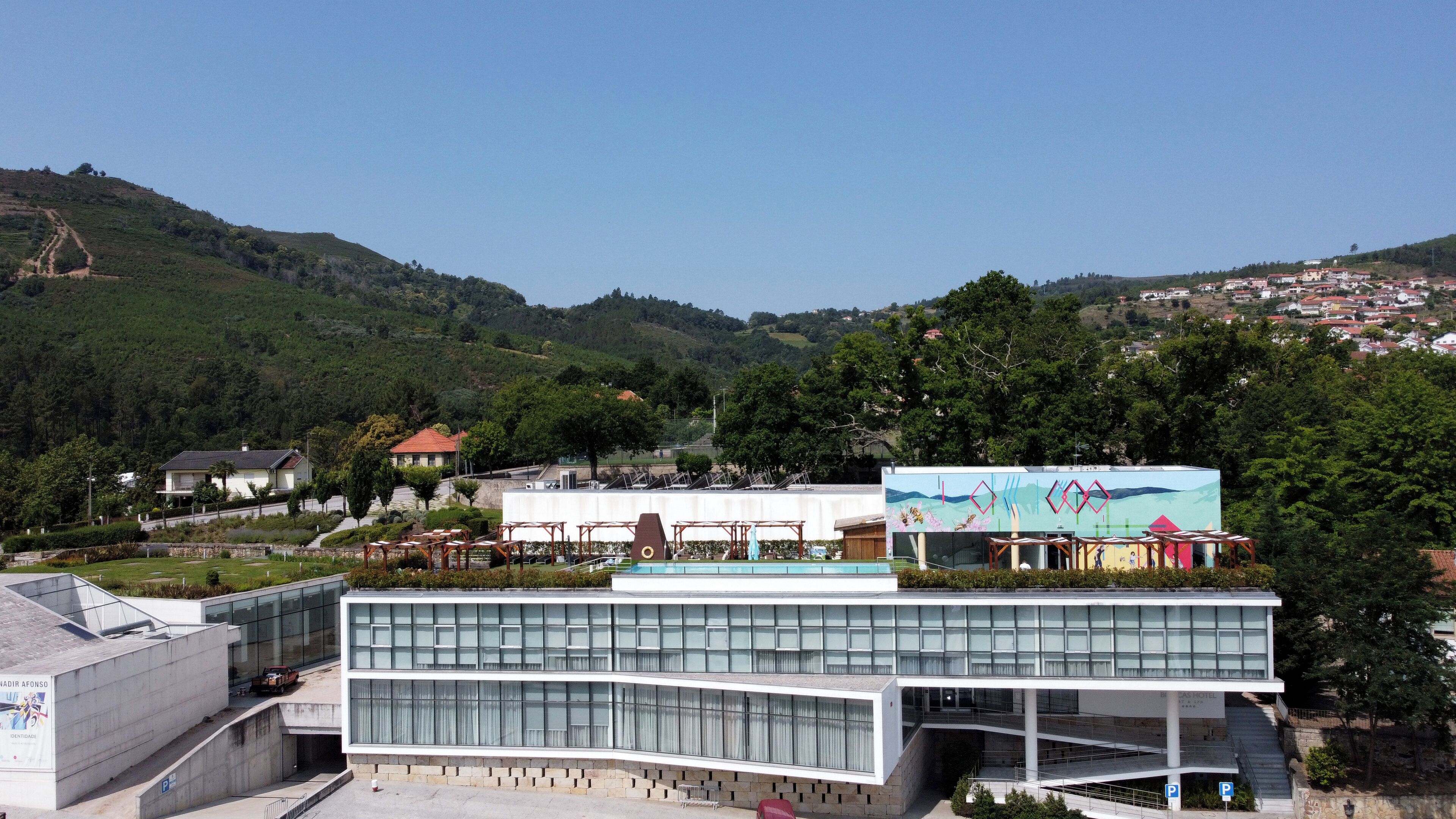 A modern hotel with a glass facade, a swimming pool, and a view of the surrounding hills.