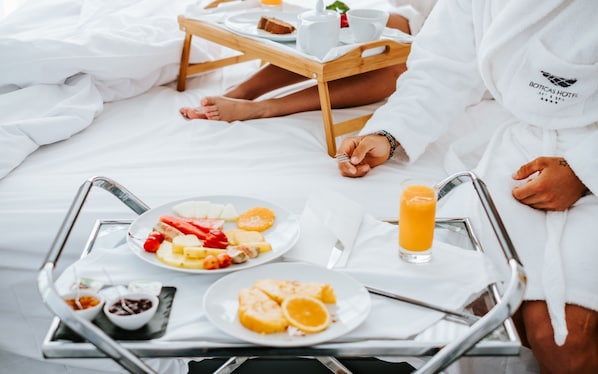 Bandeja de desayuno con frutas, un vaso de jugo de naranja y una taza sobre la cama.