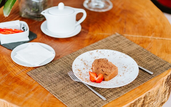 Una mesa de madera con un plato de comida, una tetera blanca y un cuenco pequeño de fresas.