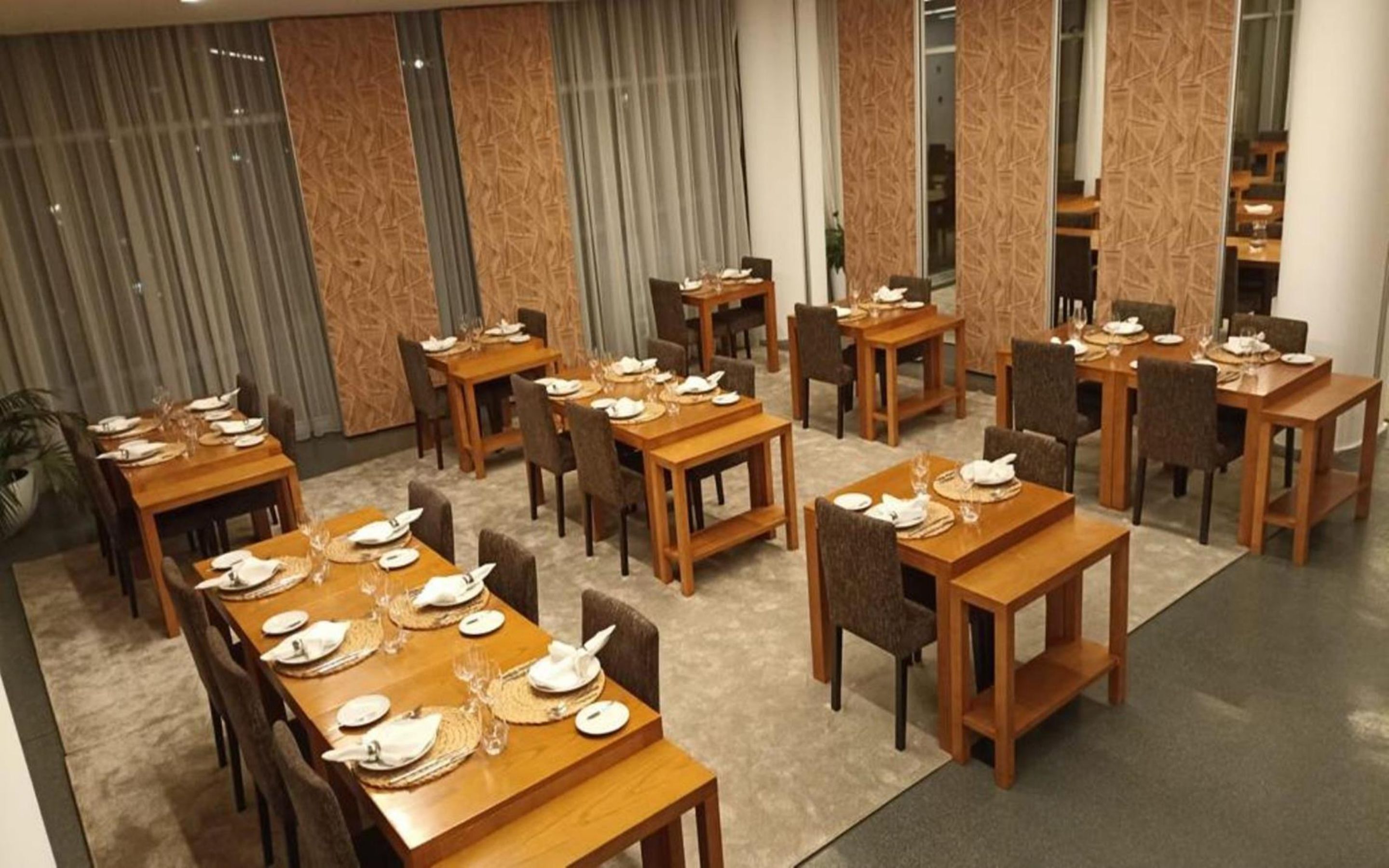 A hotel dining area with multiple wooden tables set for dining, arranged in a spacious layout.