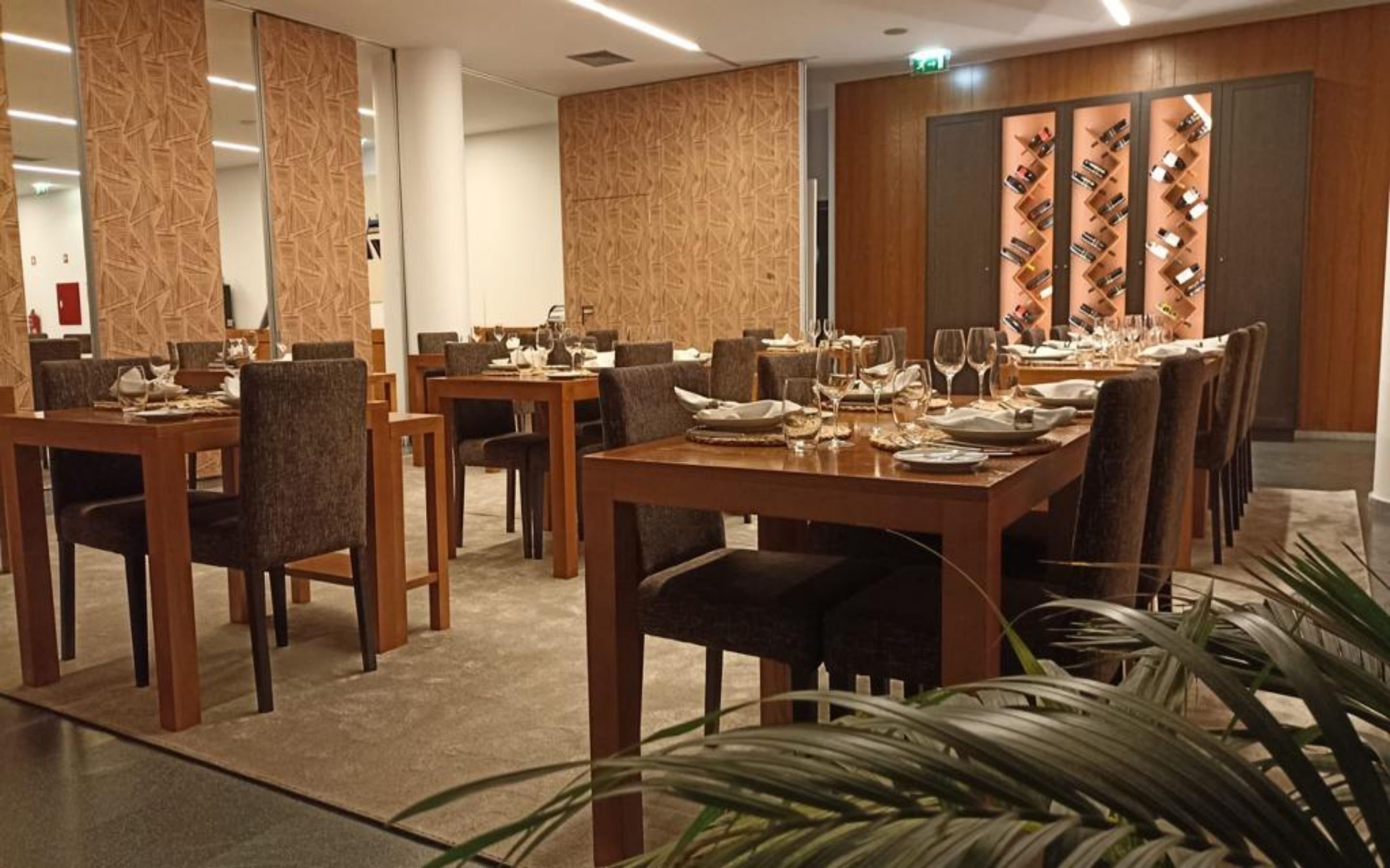 Un restaurant avec de nombreuses tables dressées pour le service, des murs lambrissés et un présentoir à vin sur le côté droit.