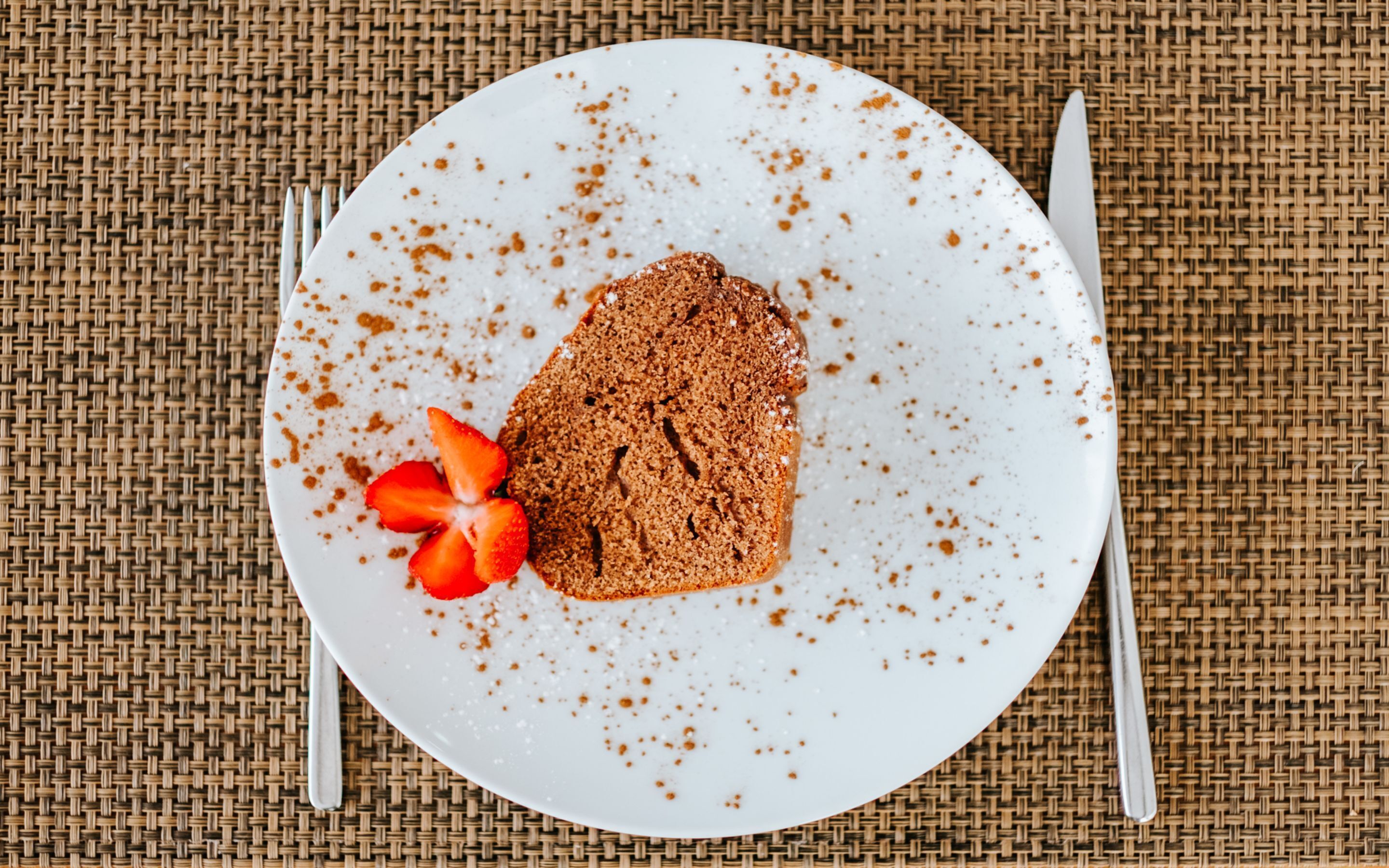 A plate with a slice of cake and a strawberry on a woven mat.