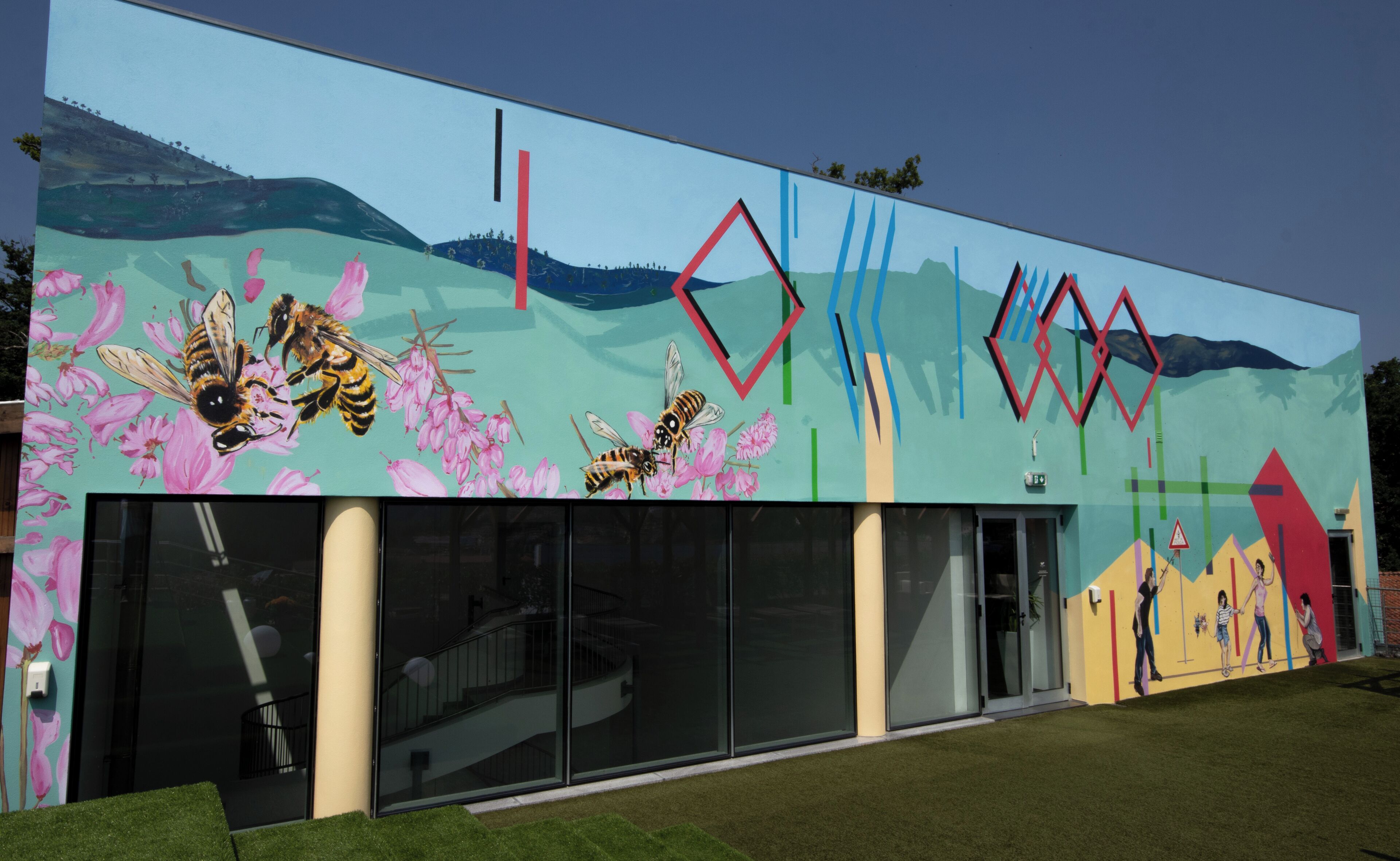 A modern building with a mural of bees and flowers, large glass windows, and a geometric design on the facade.