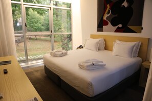 A hotel room with a large bed, a desk, and a window offering a view of trees. - Boticas Hotel Art & Spa (Boticas)
