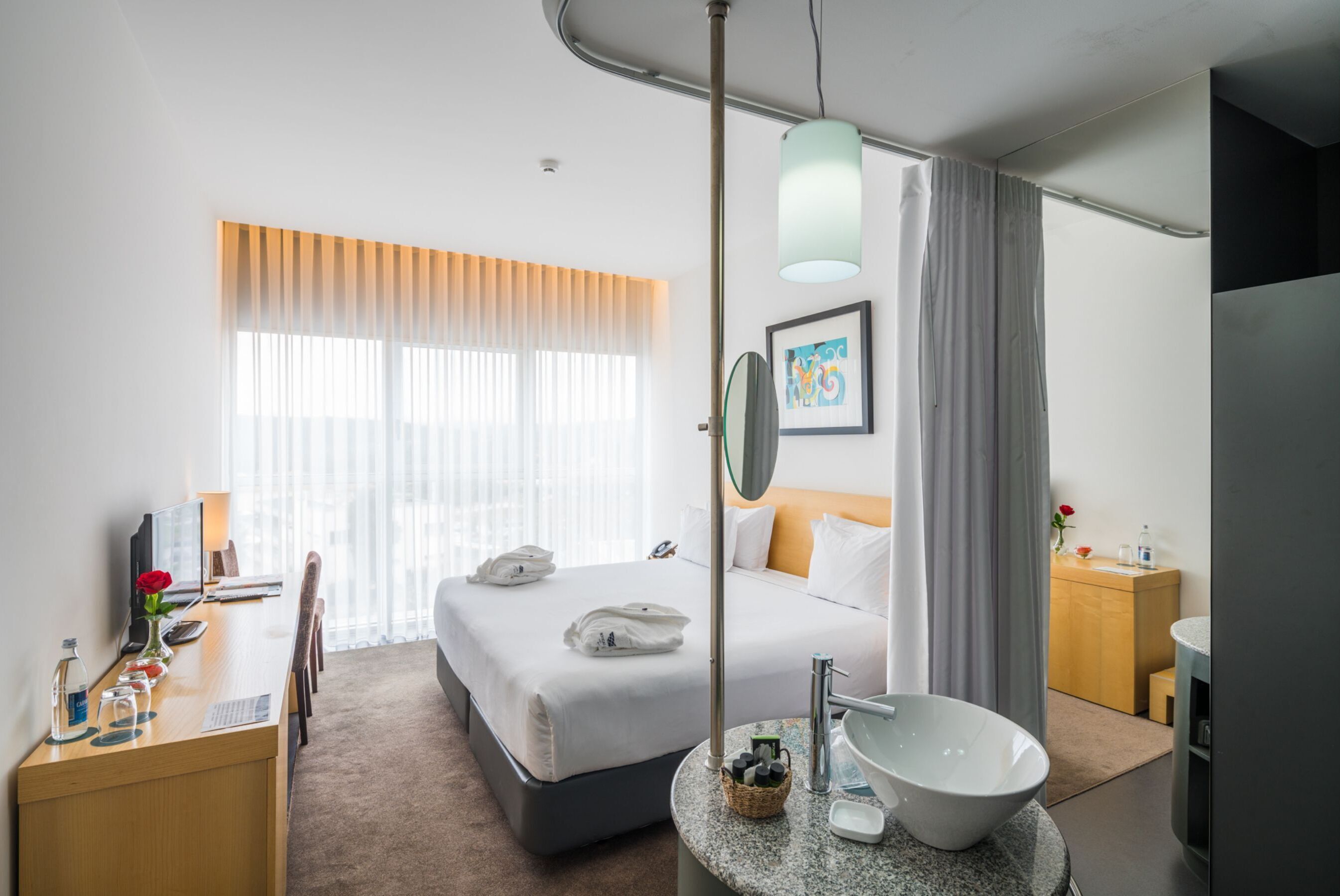 Habitación de hotel con cama, escritorio y lavamanos de mármol redondo.